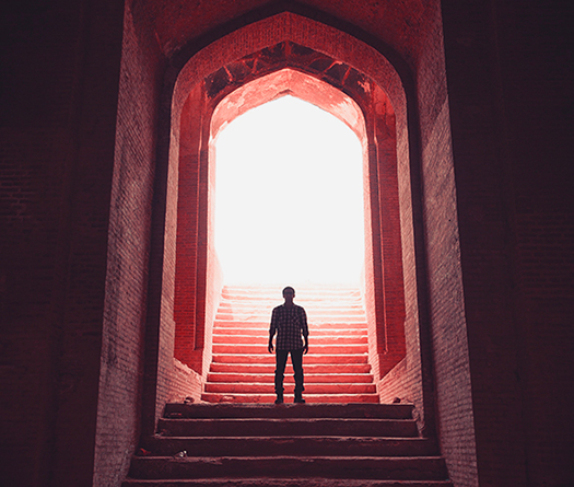 Person standing on stairs with a giant arch and light behind him to illustrate interintstutional partnerships for students at McGil