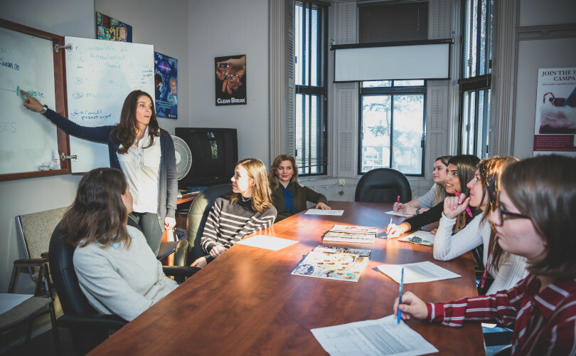 A person standing in front of a group of people sitting around a table