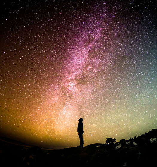 A person standing on a hill looking at the stars