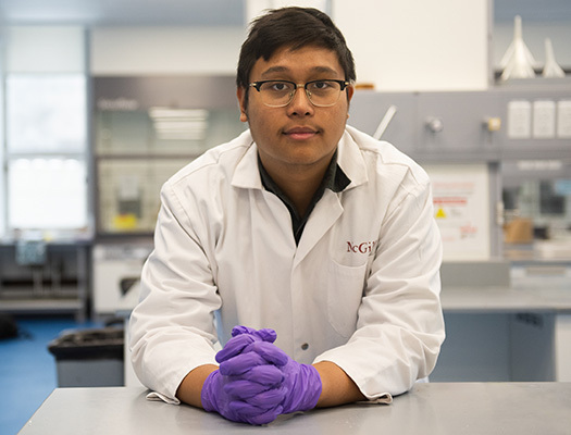 A man wearing glasses, a white lab coat and purple gloves