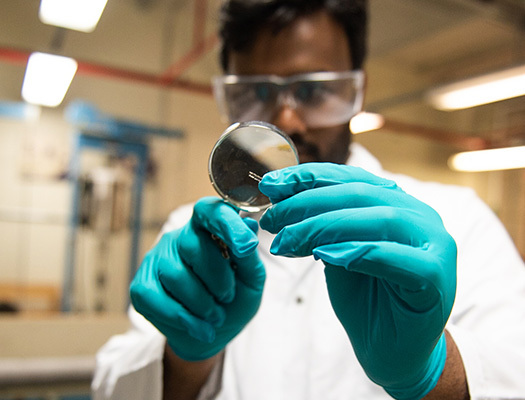 A man in a white lab coat looking at something with a magnifying glass