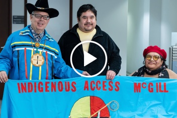 Three members of Indigenous Access McGill holding a blue banner.