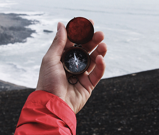 Hand holding a compass with view of the ocean to show preparing future-ready students to be engaged and global citizens