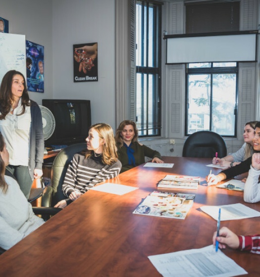 A person standing in front of a group of people sitting around a table
