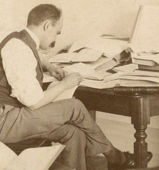 A person sitting at a desk with a pile of books.