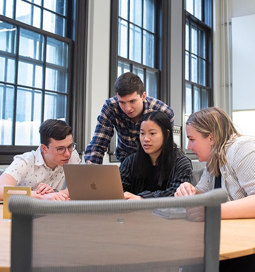 Group of four McGill students in a classroom with big windows looking at a laptop 