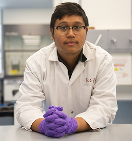 A man wearing glasses, a white lab coat and purple gloves