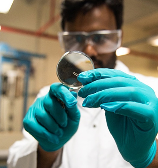 A man in a white lab coat looking at something with a magnifying glass