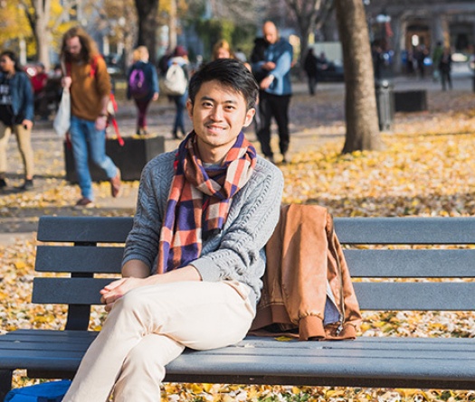 Lower campus in the autumn with student on bench with people walking on path nearby
